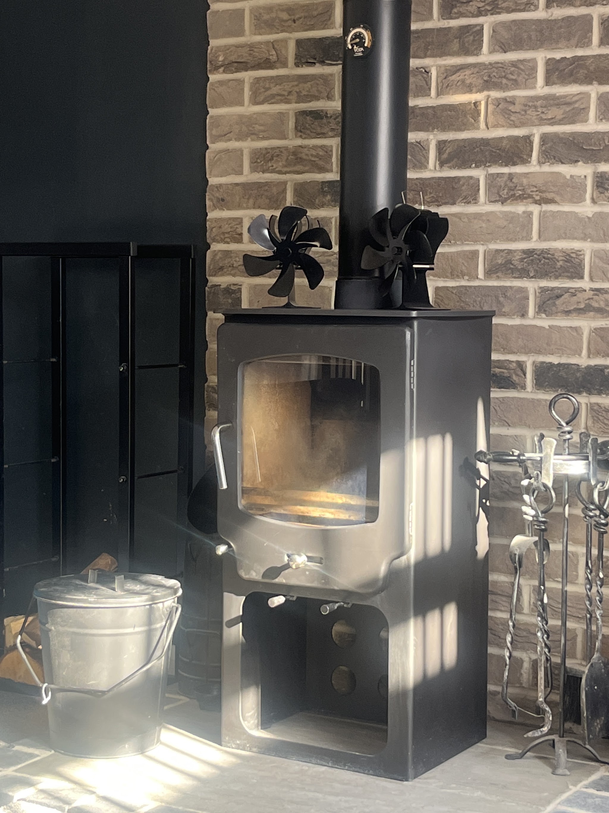 A modern black log burner with a stove fan in a brick fireplace