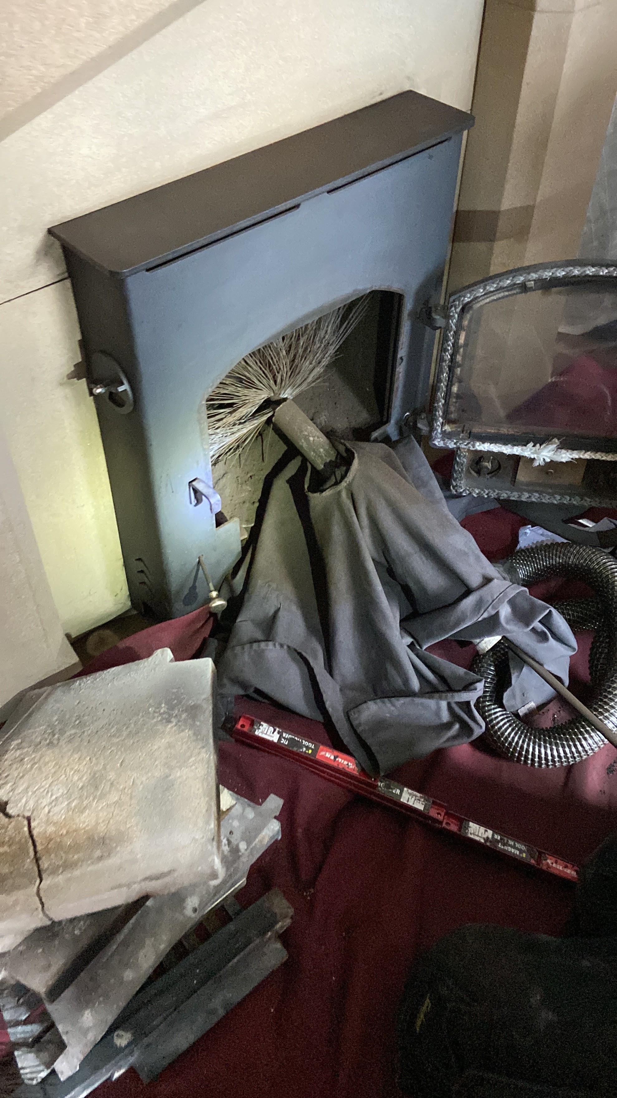 Sweep's brush coming down into an open stove, with dust sheets and a vacuum hose laid out