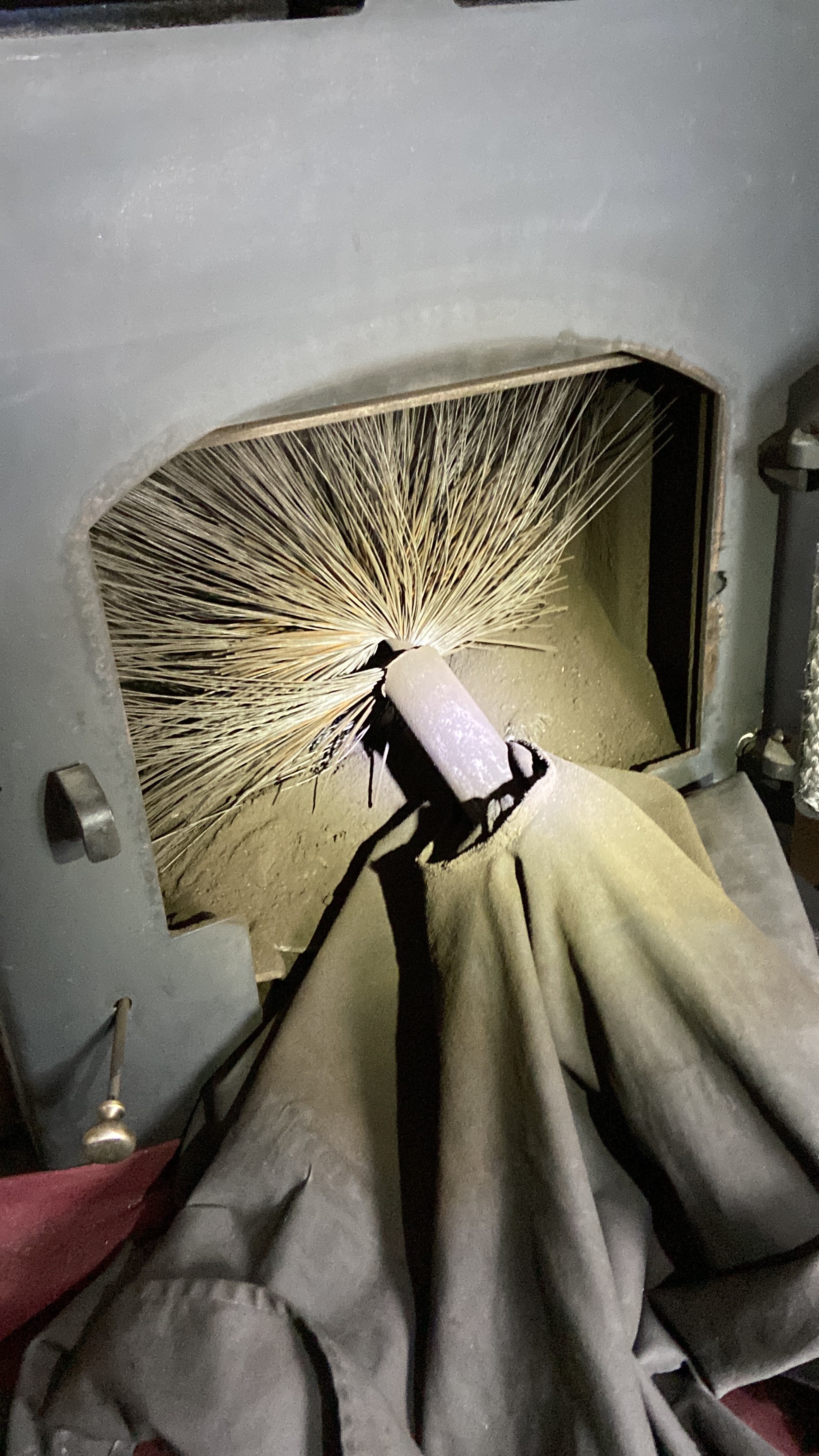 Close-up of the sweep's brush head coming into a stove firebox over a dust sheet